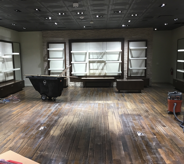 Empty retail interior mid-decommission: fixtures and millwork stripped to a whitebox state, debris staged in a tilt cart, reclaimed wood floors swept clean, ready for the next tenant build-out.
